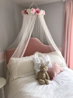 a teddy bear sitting on top of a bed with a canopy over it's head