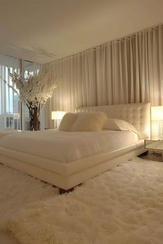 a large white bed sitting in a bedroom next to a tall window with sheer curtains