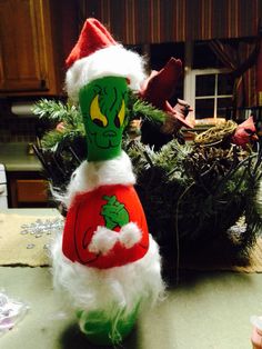 a green and red santa clause doll sitting on top of a table next to a potted plant