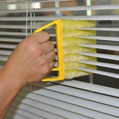 a person is cleaning the blinds with a yellow dust mop and sponge on it