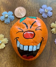 an orange painted like a clown with flowers around it and a penny on the table