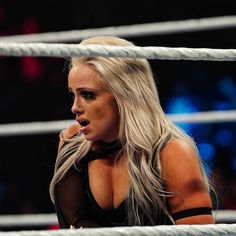 a woman with long blonde hair standing next to a wrestling ring