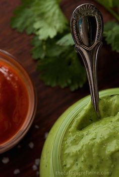 a spoon sticking out of a green bowl filled with guacamole and salsa