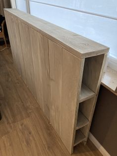 a wooden shelf with shelves on top of it in front of a window and wood flooring