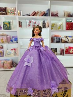 the doll is wearing a purple dress with flowers on it's skirt and stands in front of a bookshelf