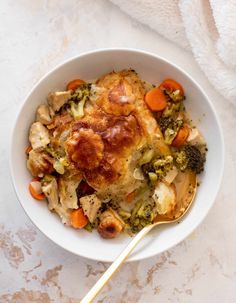 a bowl filled with broccoli, chicken and carrots next to a white towel