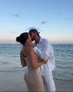 a man and woman kissing on the beach at sunset with water in the back ground