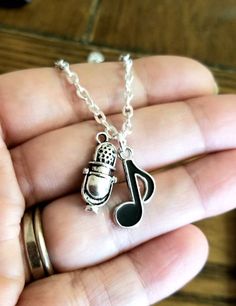 a hand holding a silver necklace with a microphone and musical note charm on it's chain