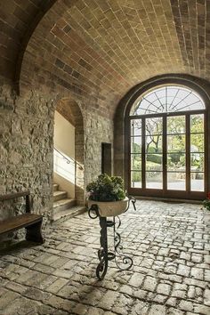 a stone building with an arched window and brick flooring, along with a wooden bench in the center