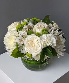 a vase filled with white and green flowers on top of a table next to a gray wall