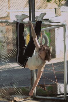 a young boy is hanging upside down on a metal pole in front of a chain link fence