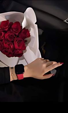 a woman's hand holding a bouquet of red roses while sitting in a car