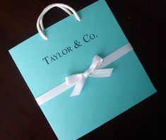 a blue gift bag with a white ribbon on it that says taylor & co in black lettering