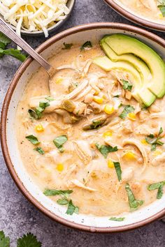 two bowls filled with chicken enchilada soup and topped with avocado