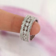 a woman's hand with a diamond ring on top of her finger in front of a pink and white background