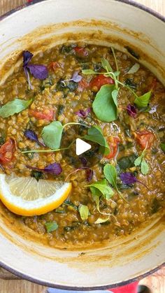 a pot filled with lentils and vegetables on top of a wooden table next to a slice of lemon