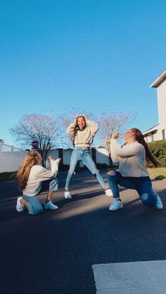 three girls are standing in the street and one girl is holding her arms out with both hands