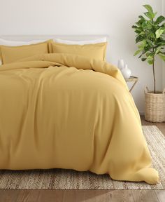 a bed with yellow sheets and pillows in a room next to a potted plant