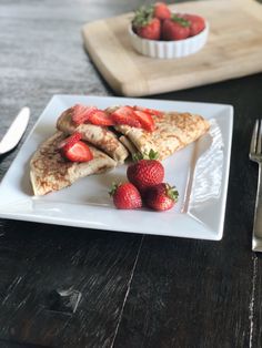 some strawberries are on a white plate next to a fork and bowl of strawberries