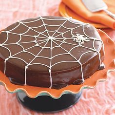 a chocolate cake with spider web decoration on top sitting on a plate next to an orange napkin