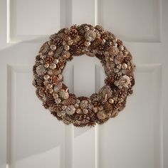 a wreath hanging on the front door of a white house with pine cones and other decorations