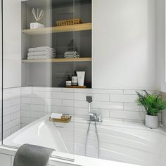 a white bath tub sitting next to a bathroom sink under a mirror with shelves above it