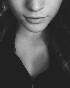 a black and white photo of a young woman with piercings on her nose looking at the camera