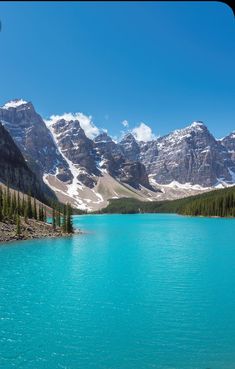 a lake surrounded by mountains and trees with blue water in the foreground on a sunny day