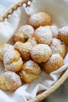 powdered sugar covered donuts in a basket on top of a cloth napkin,