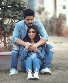 a man and woman sitting on the ground in front of a potted plant with their arms around each other