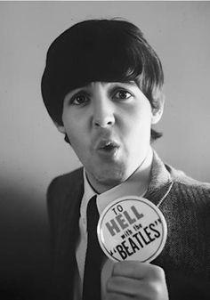 black and white photograph of a man holding up a button that says hell with the beatles