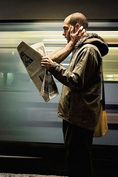 a man standing in front of a train while reading a newspaper