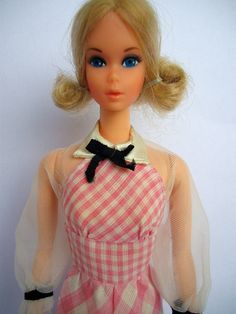 a doll wearing a pink and white dress with a black bow on the neckline