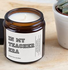 a candle sitting next to a potted plant on a wooden table with the words in my teacher's era written on it