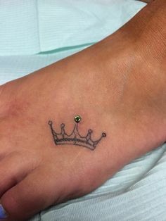 a foot with a small crown tattoo on it's side and a green jewel in the middle