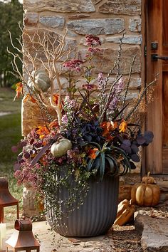 a large pot filled with lots of flowers next to a stone wall and pumpkins