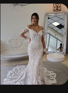 a woman standing in front of a mirror wearing a wedding dress with off the shoulder sleeves