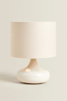 a white table lamp with a cream shade on it's base and a light bulb in the middle