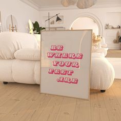 a white couch sitting on top of a hard wood floor next to a framed poster