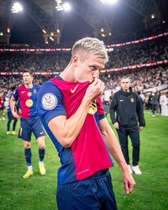 a man standing on top of a soccer field holding his hand to his mouth while wearing a red and blue shirt