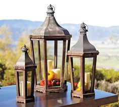 three lit up lanterns sitting on top of a wooden table in front of a mountain