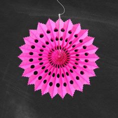 a pink paper fan with black dots hanging from a hook on a wall in the shape of a flower