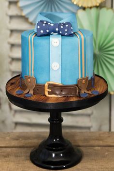 a blue cake with a bow and suitcase decoration on the top is sitting on a table