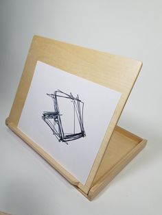 a wooden frame with a drawing in it on top of a white table next to a pen and paper