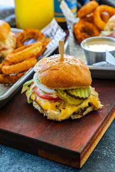 a cheeseburger with onion rings on a cutting board next to other food items