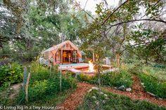 a small wooden cabin in the woods with a fire pit on the ground and trees around it