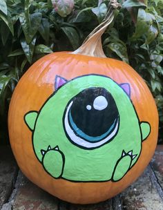 a green monster painted on a pumpkin sitting in front of some bushes and plants,