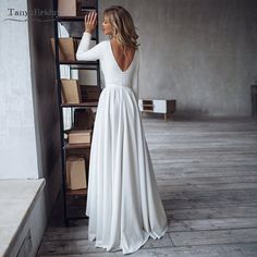 a woman in a white dress is looking at the back of her dress, and she's wearing a long sleeved gown