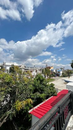 a red roof on top of a building next to some trees and clouds in the sky