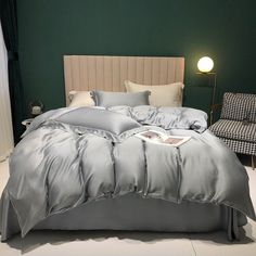 a bed with grey comforter and pillows in a green room next to a chair